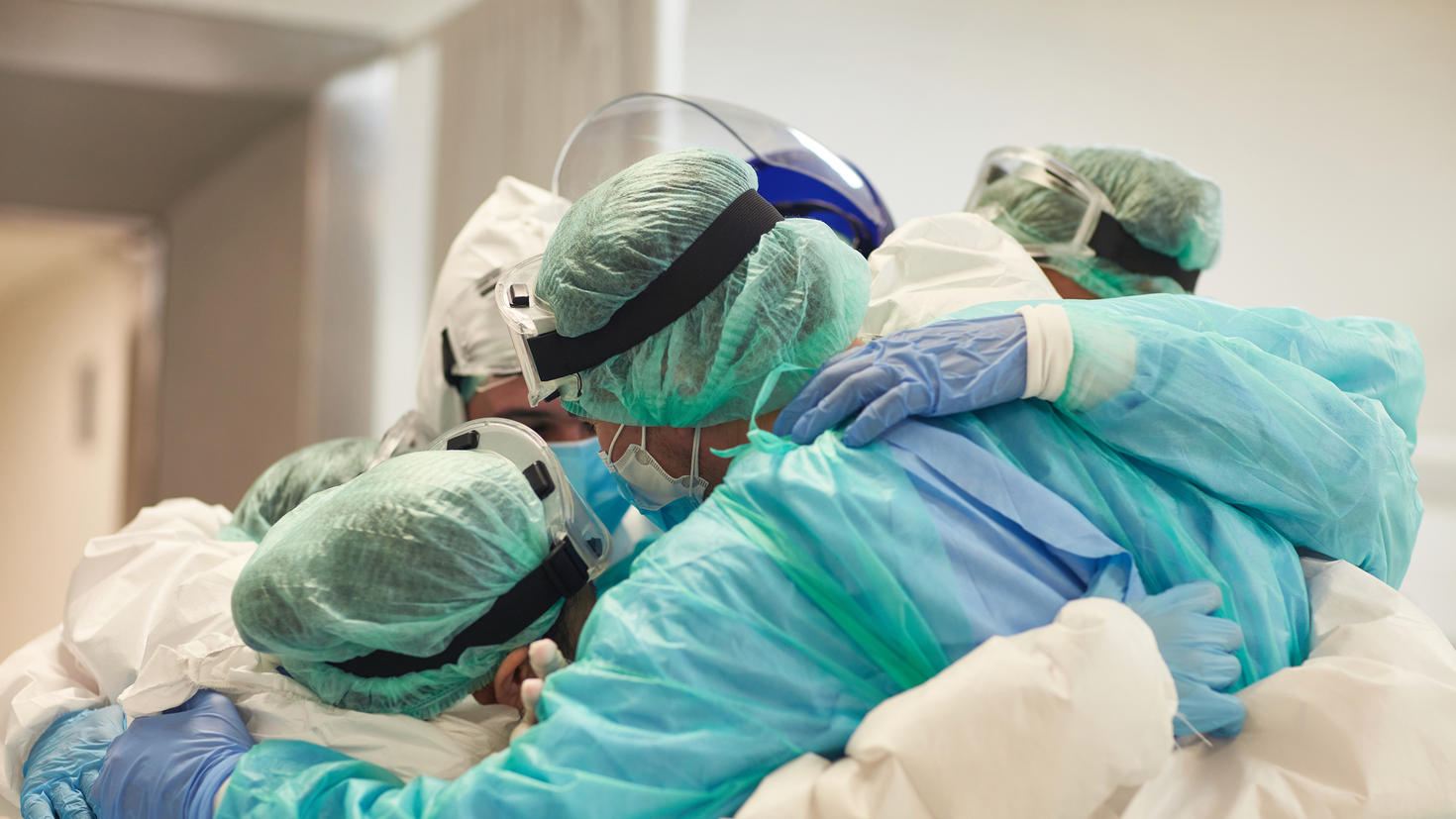 Vue partielle d'une équipe hospitalière composée d'hommes et de femmes en tenue de protection, se tenant ensemble dans une accolade.