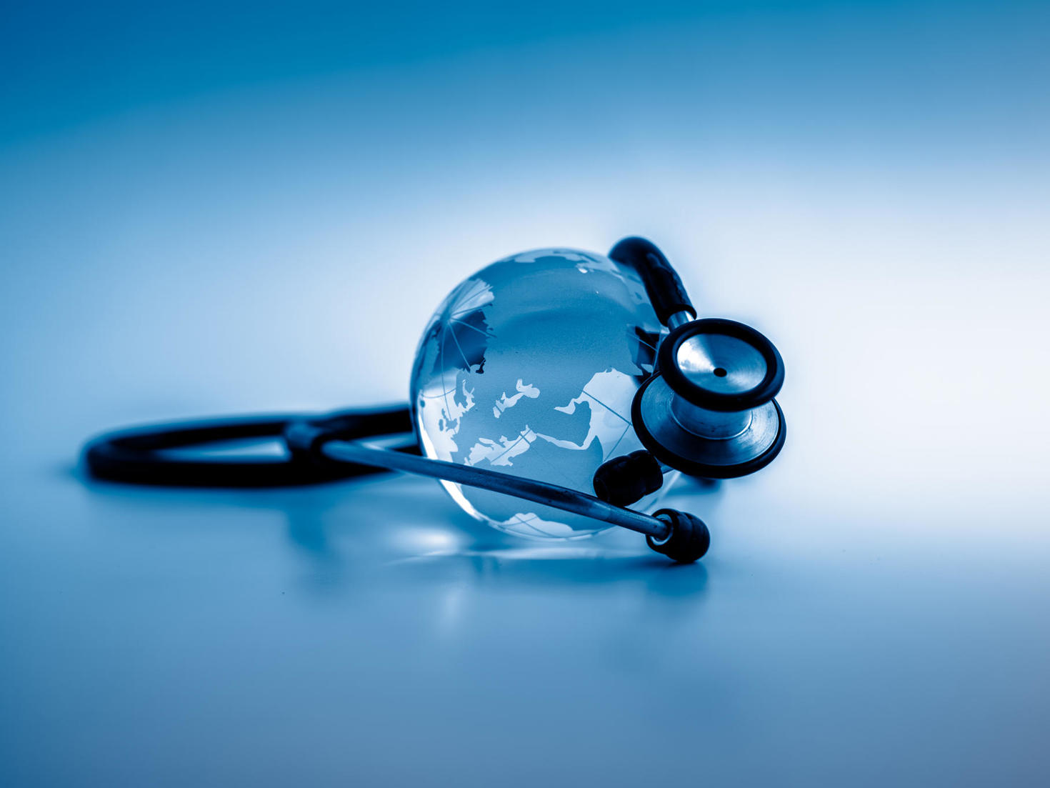 Globe terrestre reposant sur la membrane d’un stéthoscope sur un fond vert médical, symbolisant la santé mondiale, les soins de santé internationaux et la santé des populations.