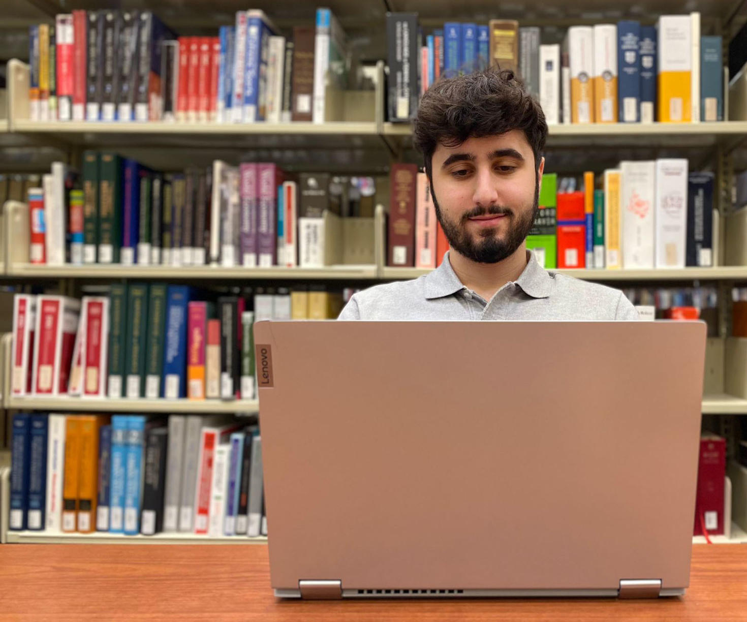 Une personne travaillant sur un ordinateur devant des étagères remplies de livres.