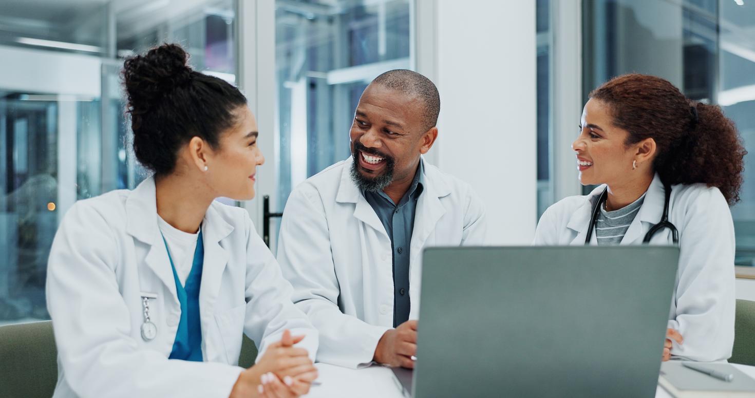 Trois médecins souriants en blouse discutent et collaborent autour d'un ordinateur portable.