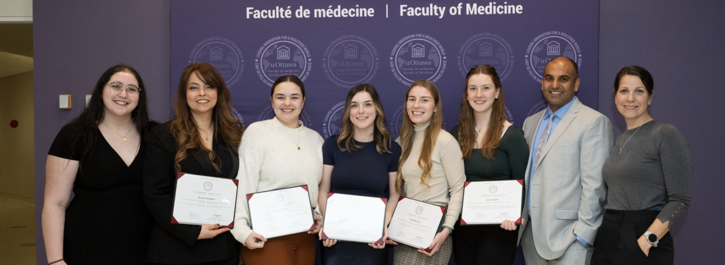 Huit personnes debout en rang devant une toile de fond de la Faculté de médecine, dont cinq tiennent un certificat.