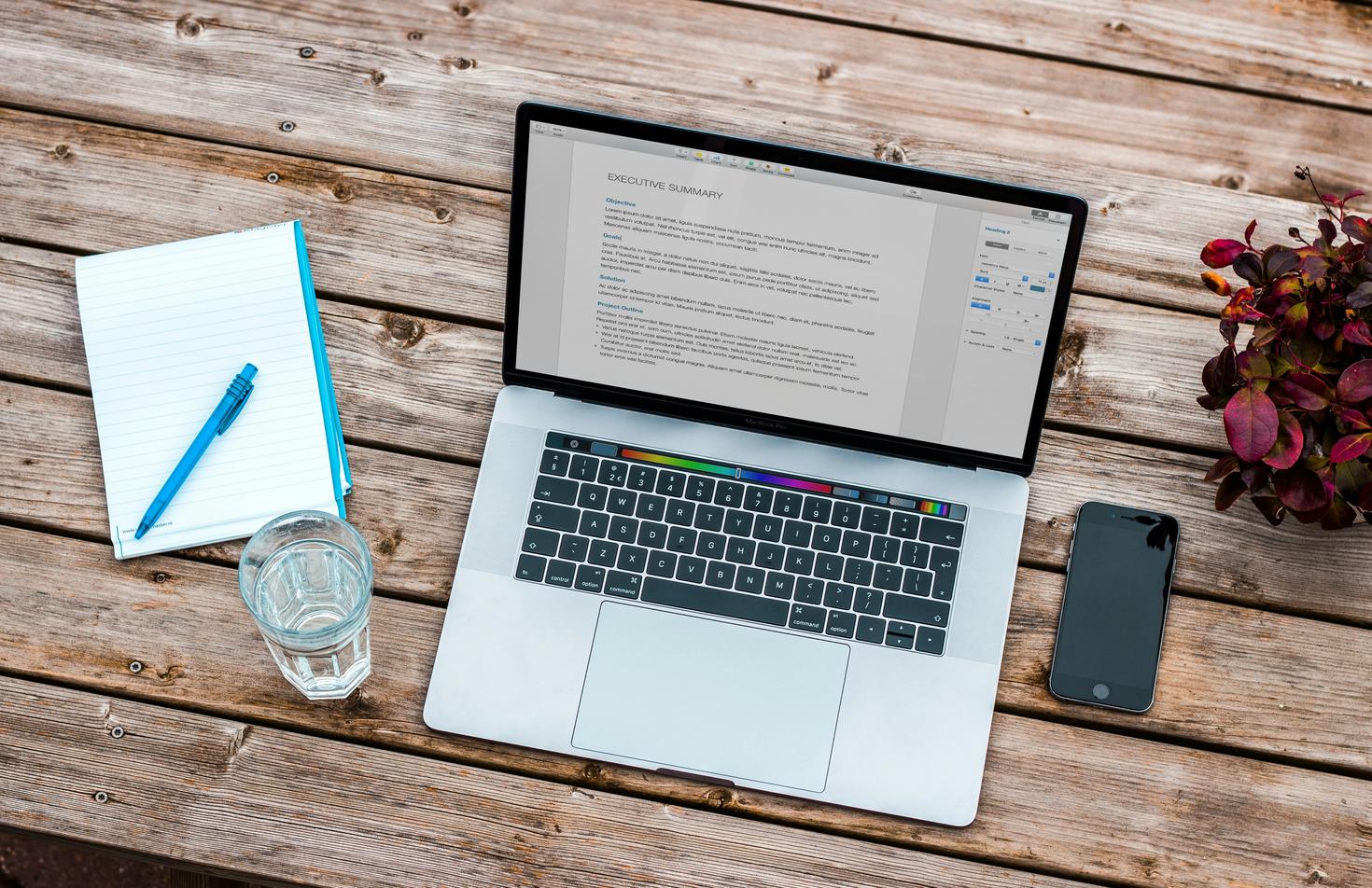 Ordinateur portable, téléphone, stylo et papier sur une table avec un verre d’eau
