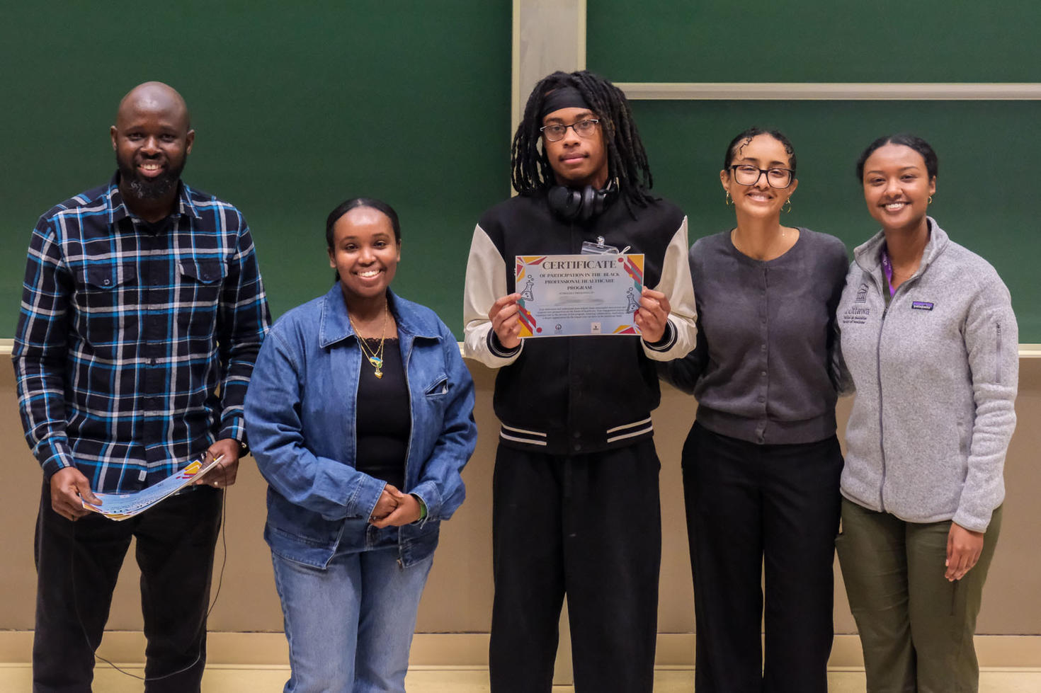 Un conseiller en orientation et trois personnes étudiantes en enseignement entourent une personne étudiante tenant un certificat de participation.