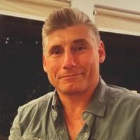 Le Dr Jason Trickovic, vêtu d'une chemise verte à col, devant un mur noir