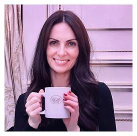 La Dre Michelle Prentice sourit en tenant une tasse blanche devant un mur rose pâle.