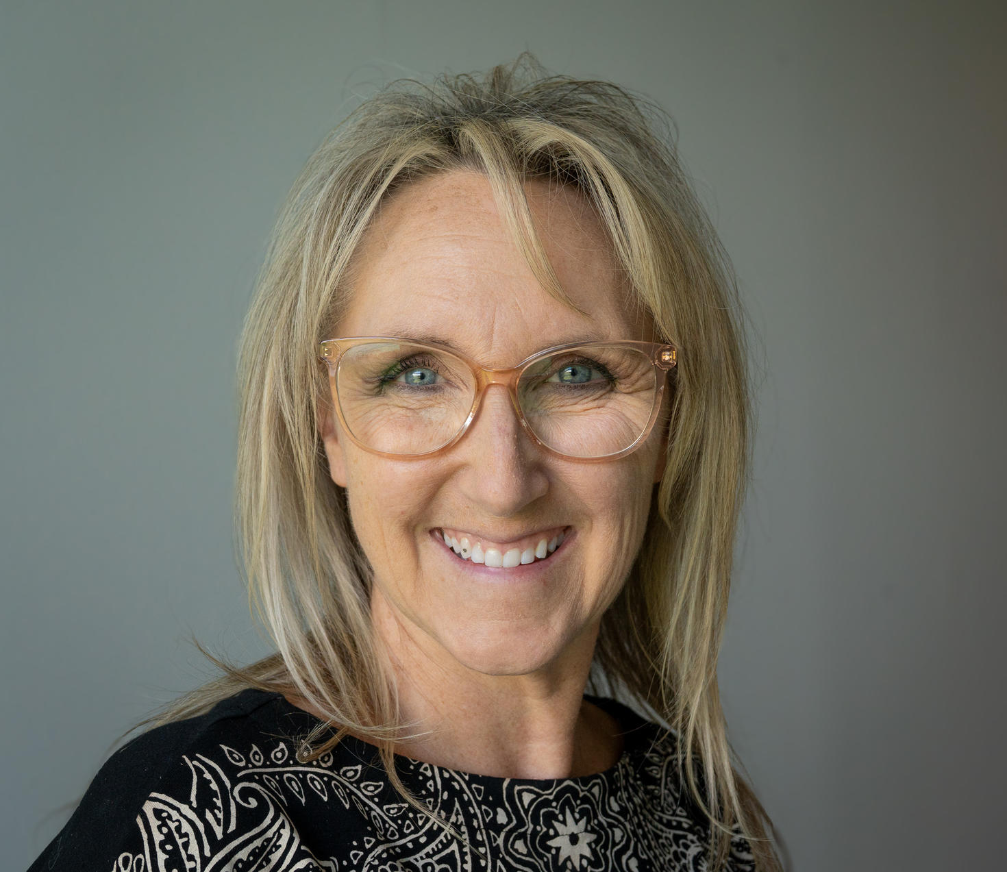 Kim Rozon, gestionnaire des programmes d’éducation, sourit et porte un haut noir orné d’un motif blanc perlé. Elle pose devant un arrière-plan gris ardoise.