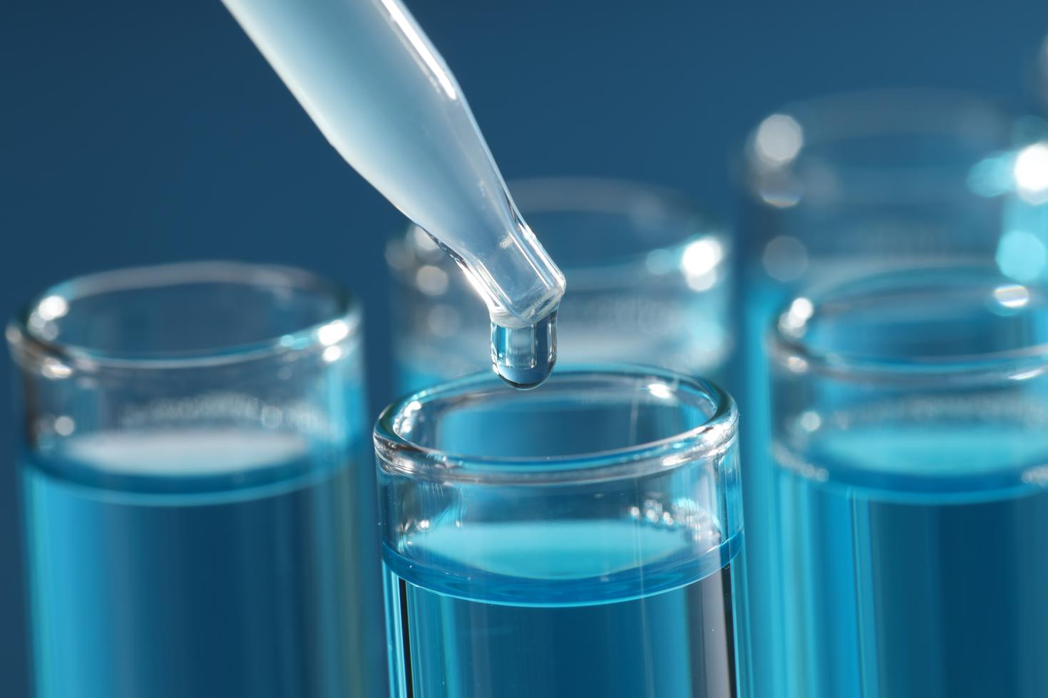 Une pipette distribue un liquide dans des fioles de laboratoire contenant une solution bleue dans un environnement de recherche.