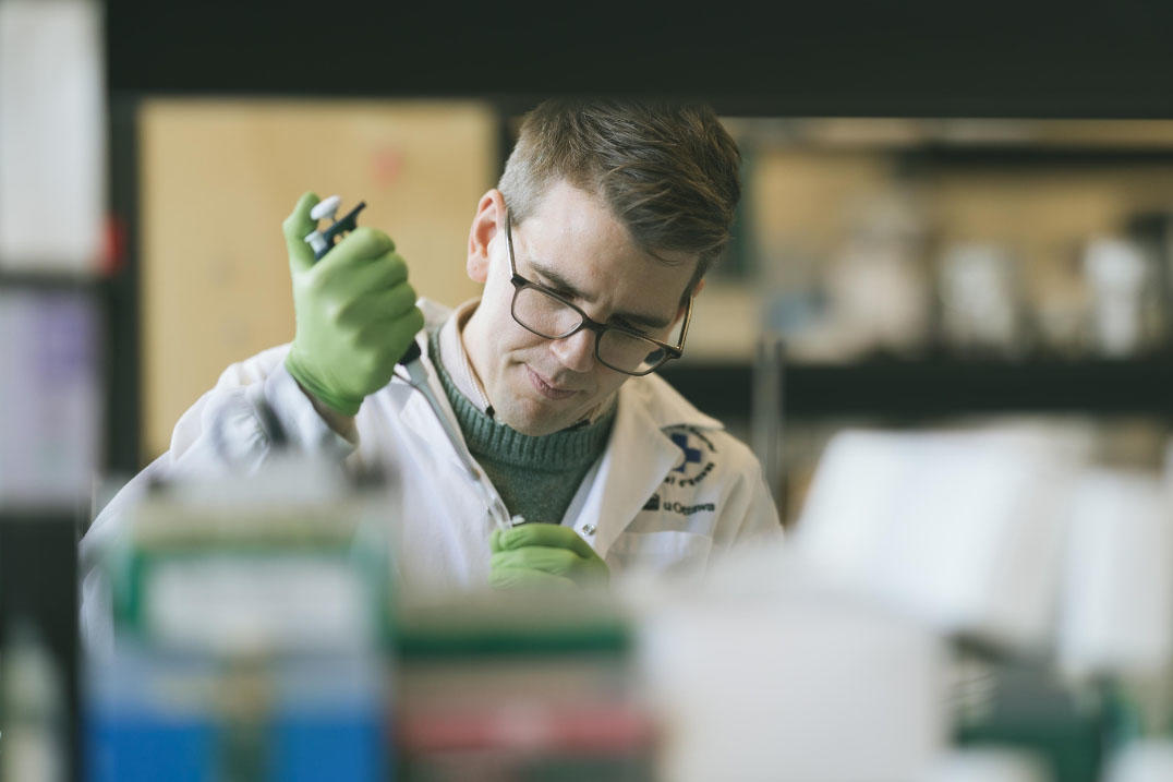 Un scientifique assis à une paillasse de laboratoire utilise une pipette pour verser une substance dans un tube.