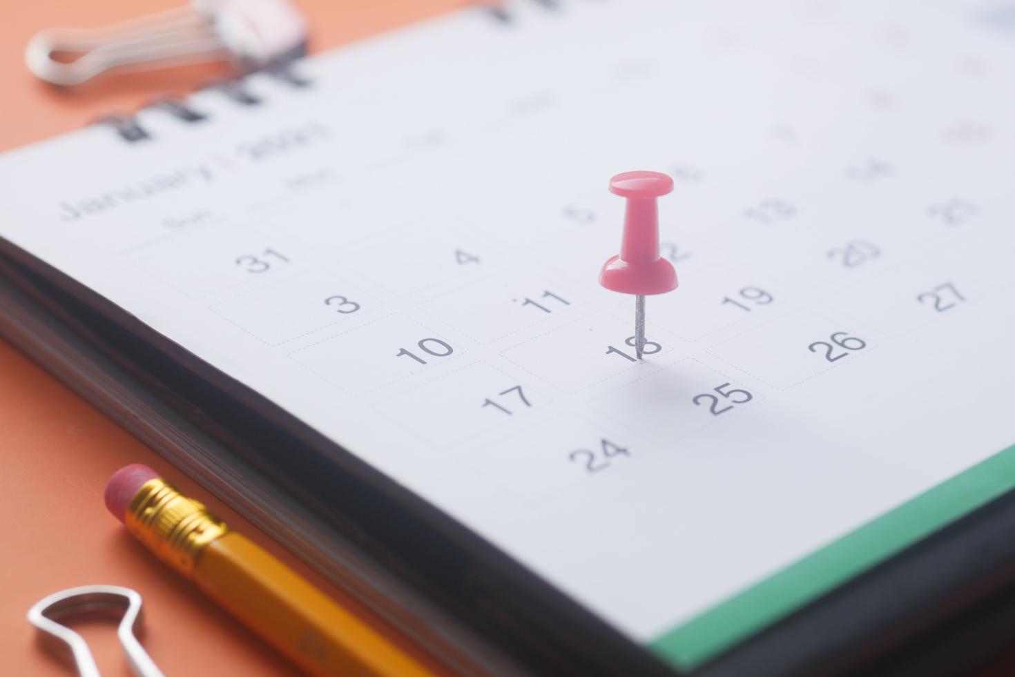 Calendrier papier avec une punaise rose marquant une date d'échéance importante