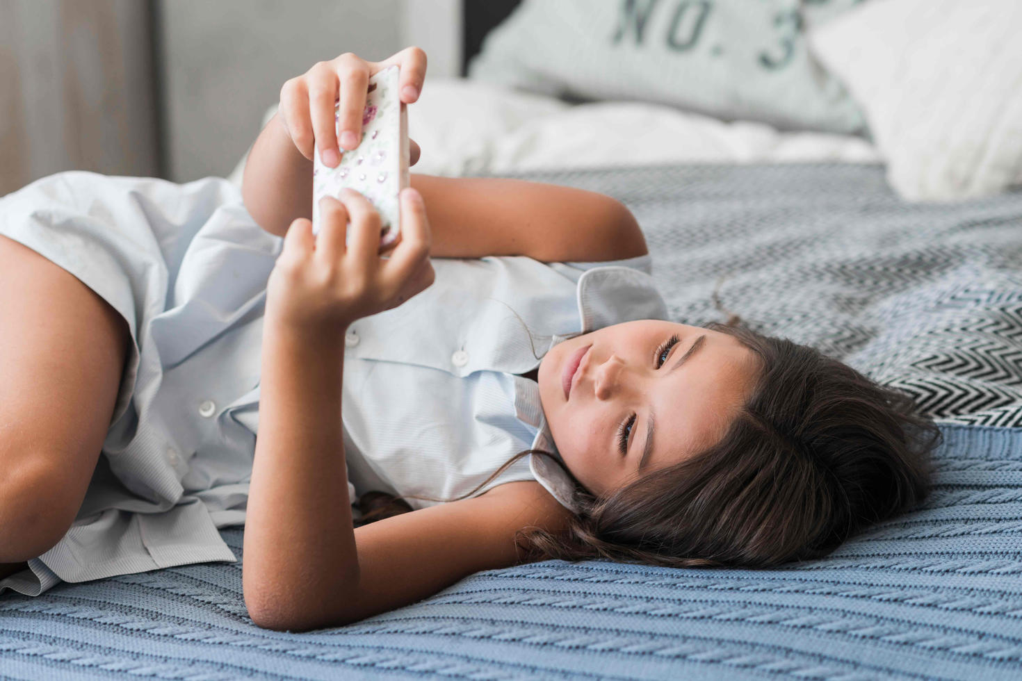 Une jeune fille sur un lit en regardant son téléphone cellulaire.