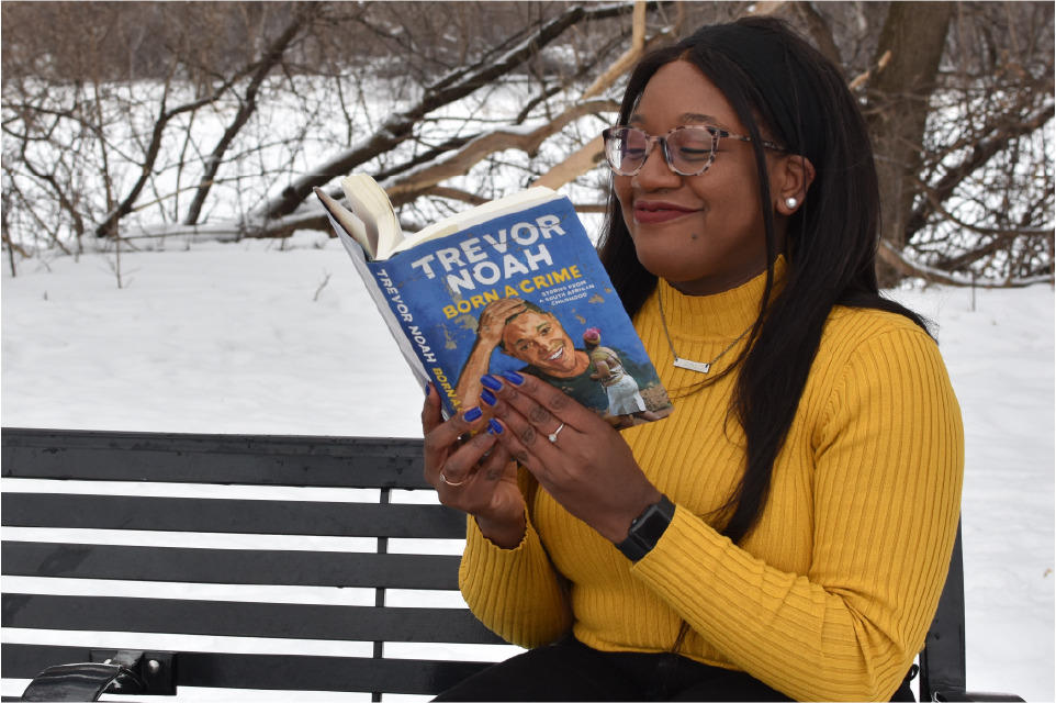 Chisom Okwor, assis sur un banc, lit le livre Born a Crime par Trevor Noah
