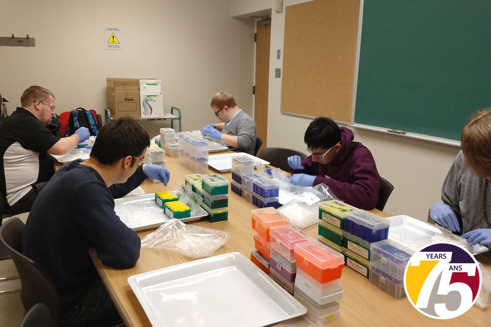 Un groupe d’hommes assis à une table dans une salle de conférence plaçant des embouts de pipette dans des boîtes.