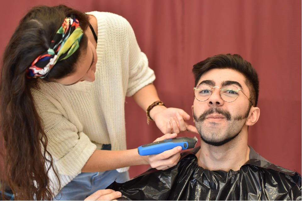 Lara Pereira shaves Ricardo Viltakis’ beard with an electric razor.