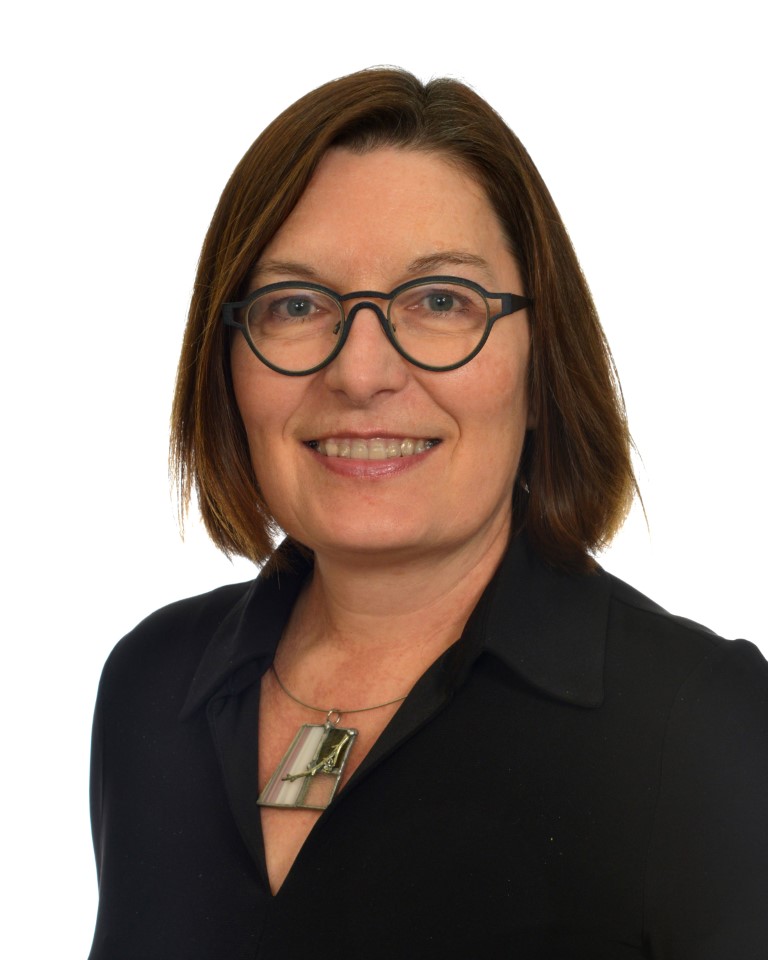 Photo de Marie Josée Drolet. Elle a des cheveux mi-longs bruns, des lunettes noires et une blouse noire. Elle sourit à la caméra.