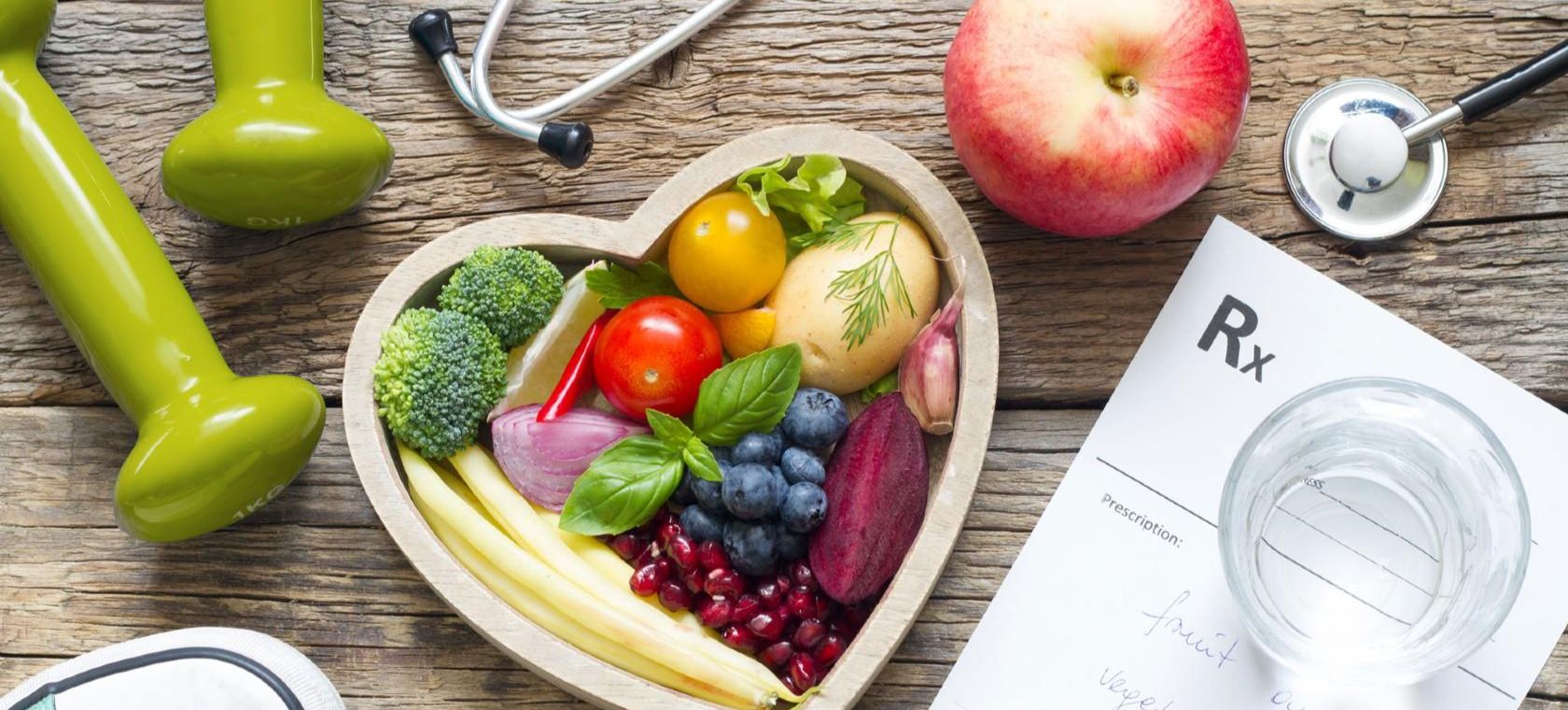 Des aliments sains dans un bol en forme de cœur, des haltères, un stéthoscope, une ordonnance et des baskets