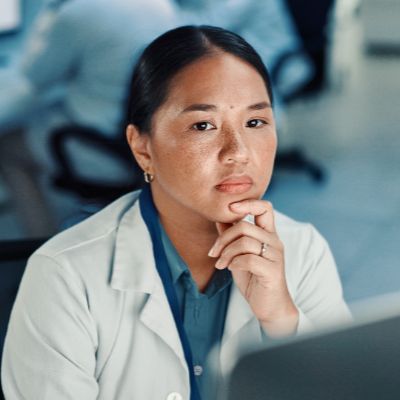 Un scientifique en blouse blanche regarde pensivement l'écran d'un ordinateur.