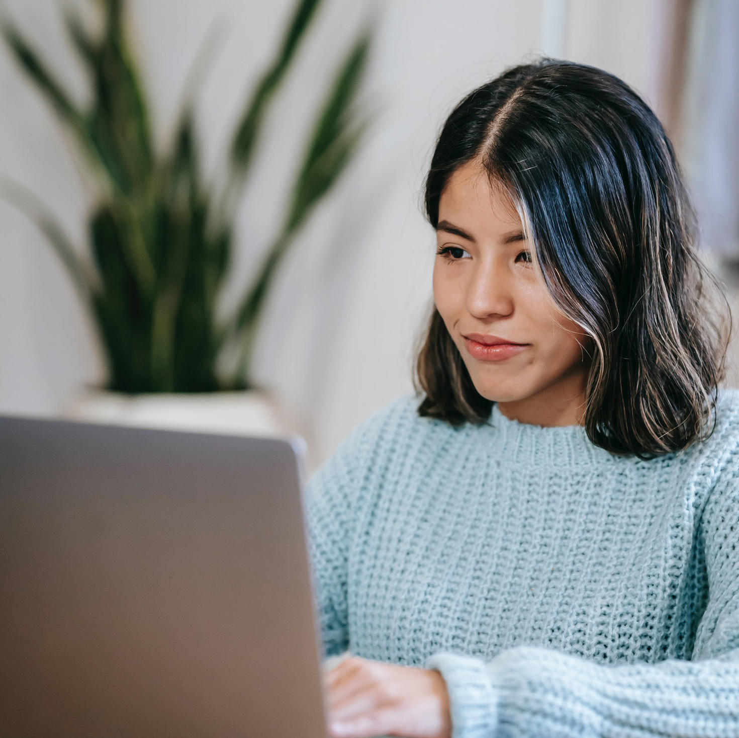 woman with glasses using a laptop with a plant in the background
