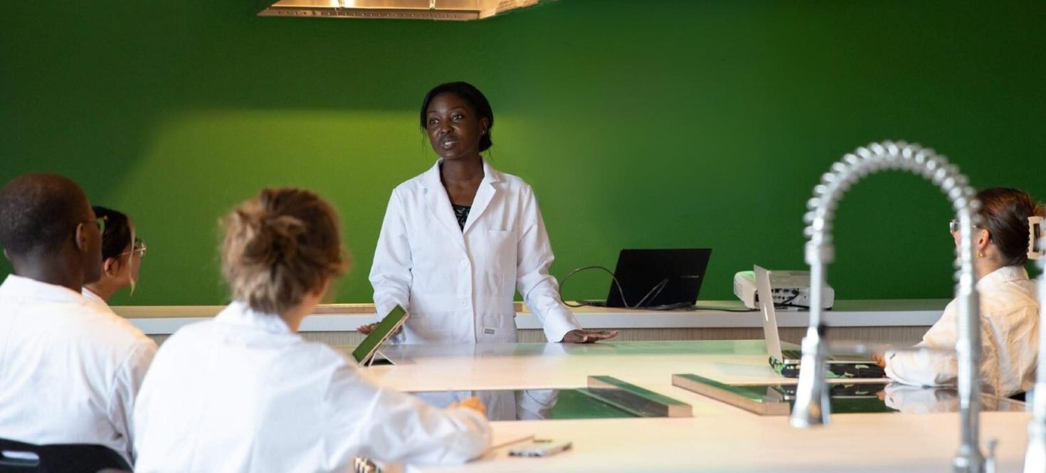 une professeure en blouse de laboratoire avec des étudiants qui la regardent
