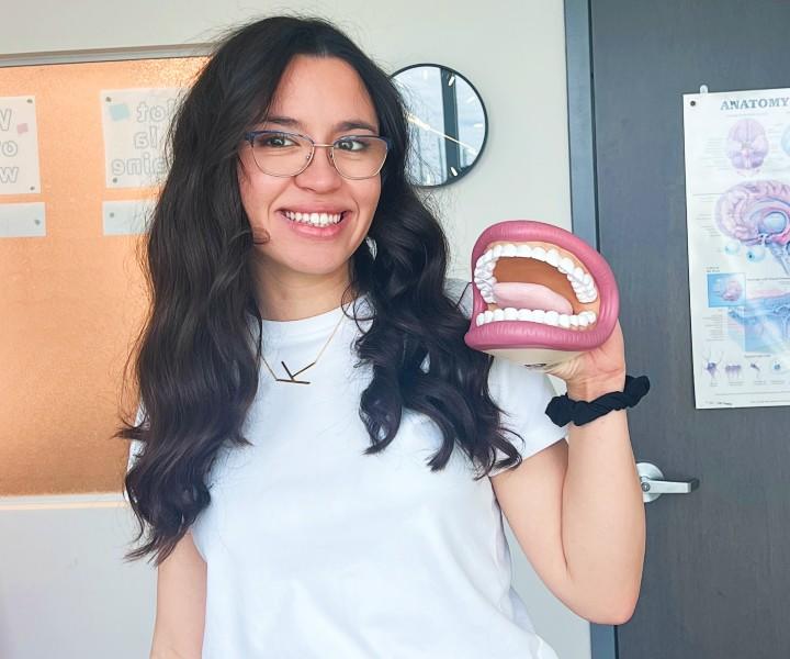Un étudiant souriant, vêtu d'un tee-shirt blanc et tenant un modèle de bouche