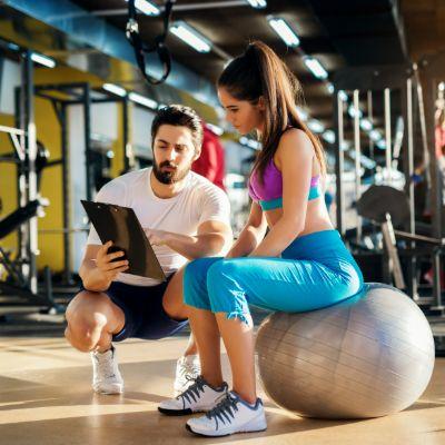 Homme et femme discutant ensemble dans une salle de musculation, l'homme a un presse-papiers
