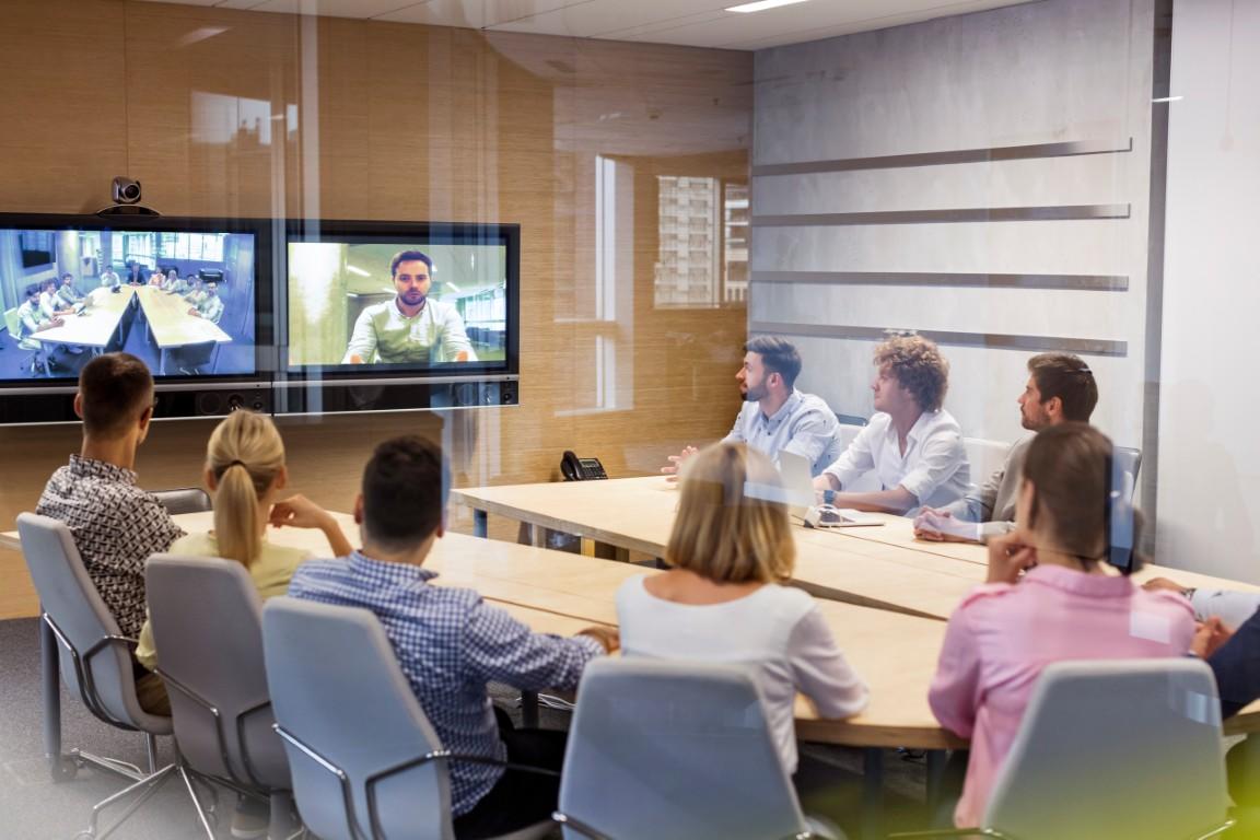Une salle de conférence avec des personnes en réunion et des personnes sur des écrans de télévision
