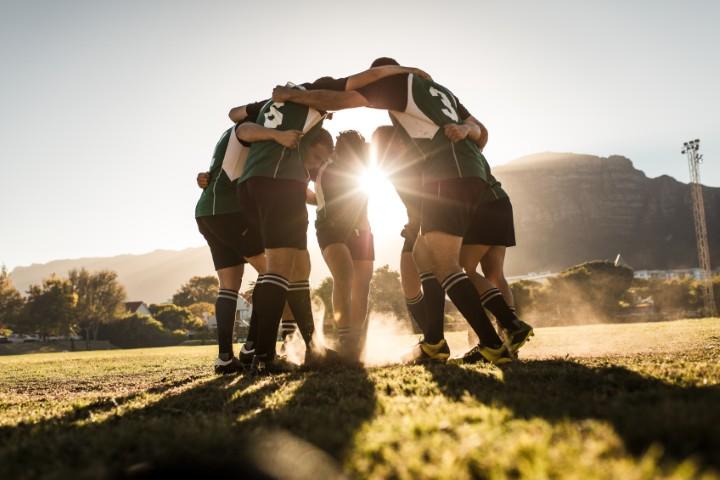 Une équipe sportive se serre les coudes avec le soleil en arrière-plan.