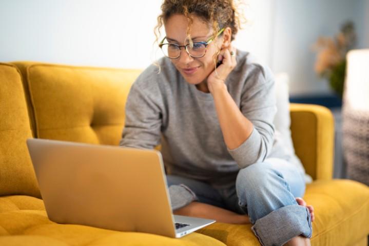 Une femme est assise sur un canapé et utilise son ordinateur portable.