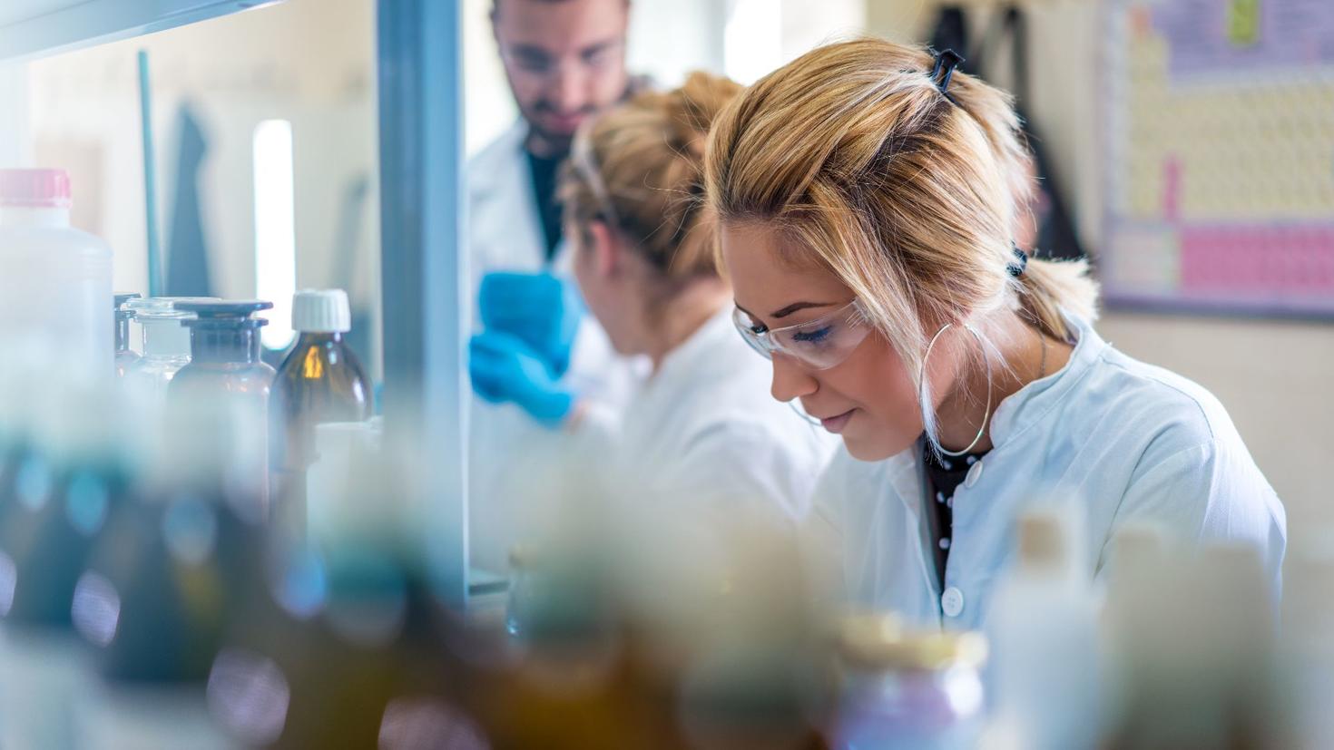 Une femme portant des lunettes de protection et souriante travaille dans un laboratoire.