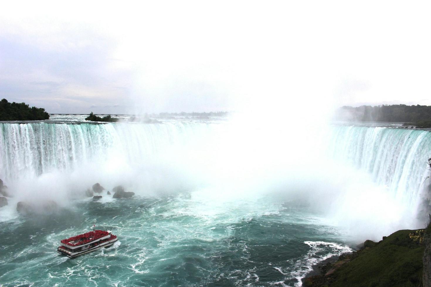 Un bateau touristique rouge transporte des passagers près du pied de la chute du Fer-à-cheval de Niagara.