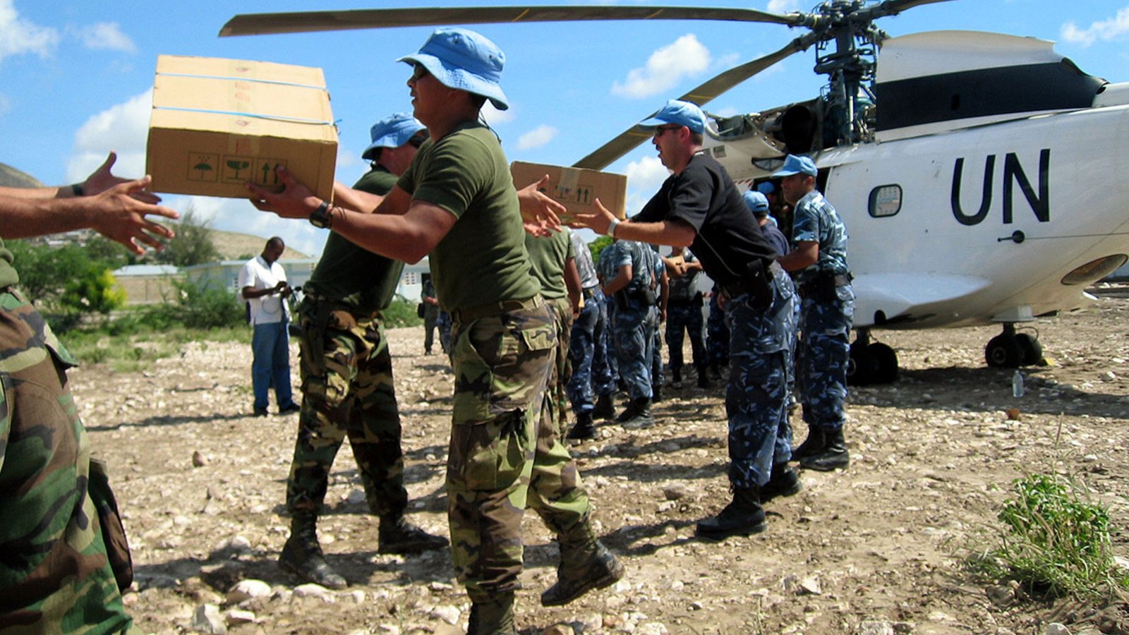 Une file de personnes en uniform en train de distribuer des boites de provisions d'un hélicoptère marqué "UN"
