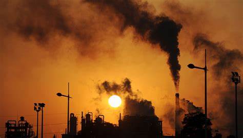 Une usine dégageant de la fumée, en arrière-plan un ciel orange lors d'un coucher de soleil
