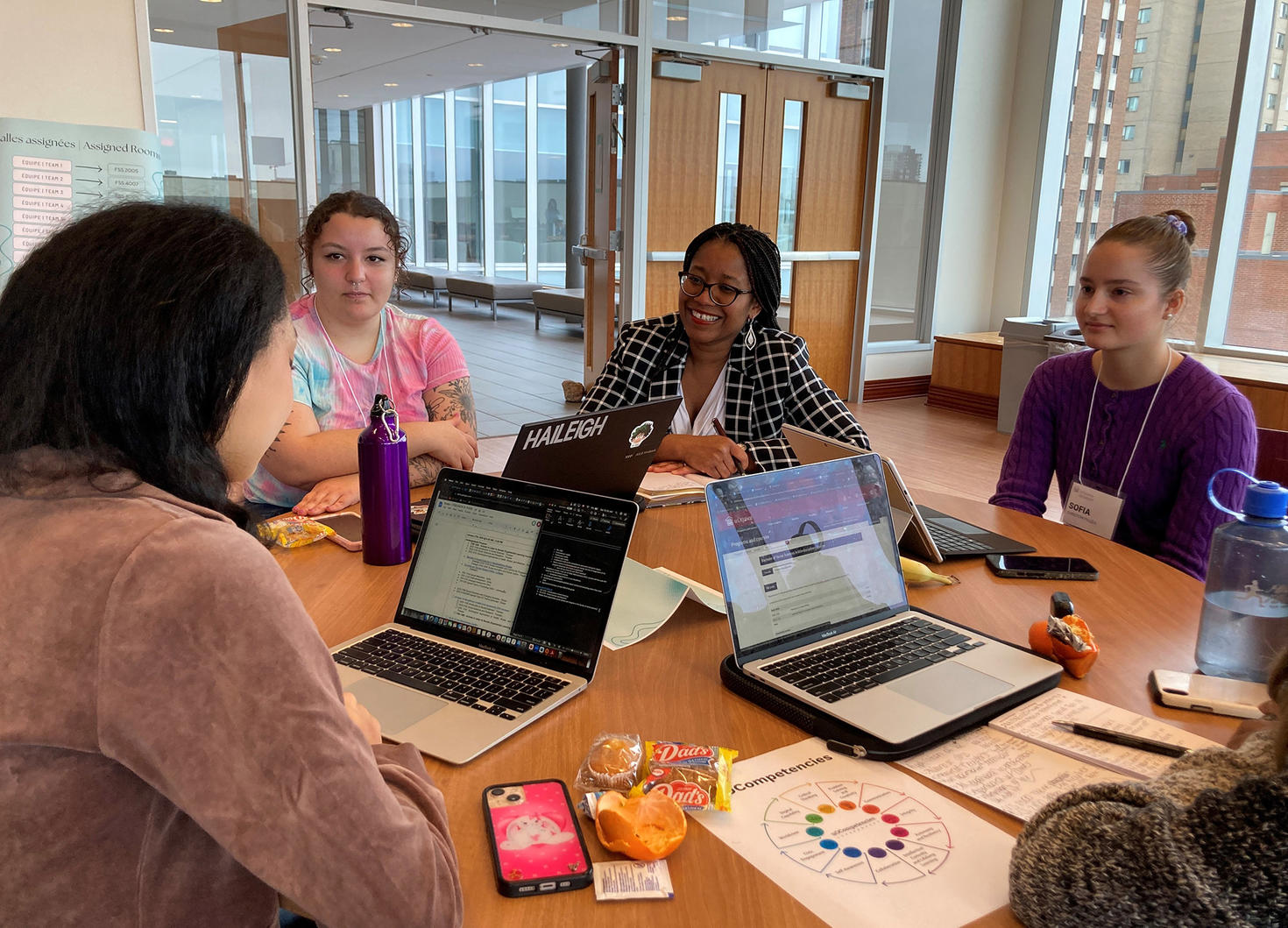 Group of female students sitting at a round table with laptops discussing with a professional.