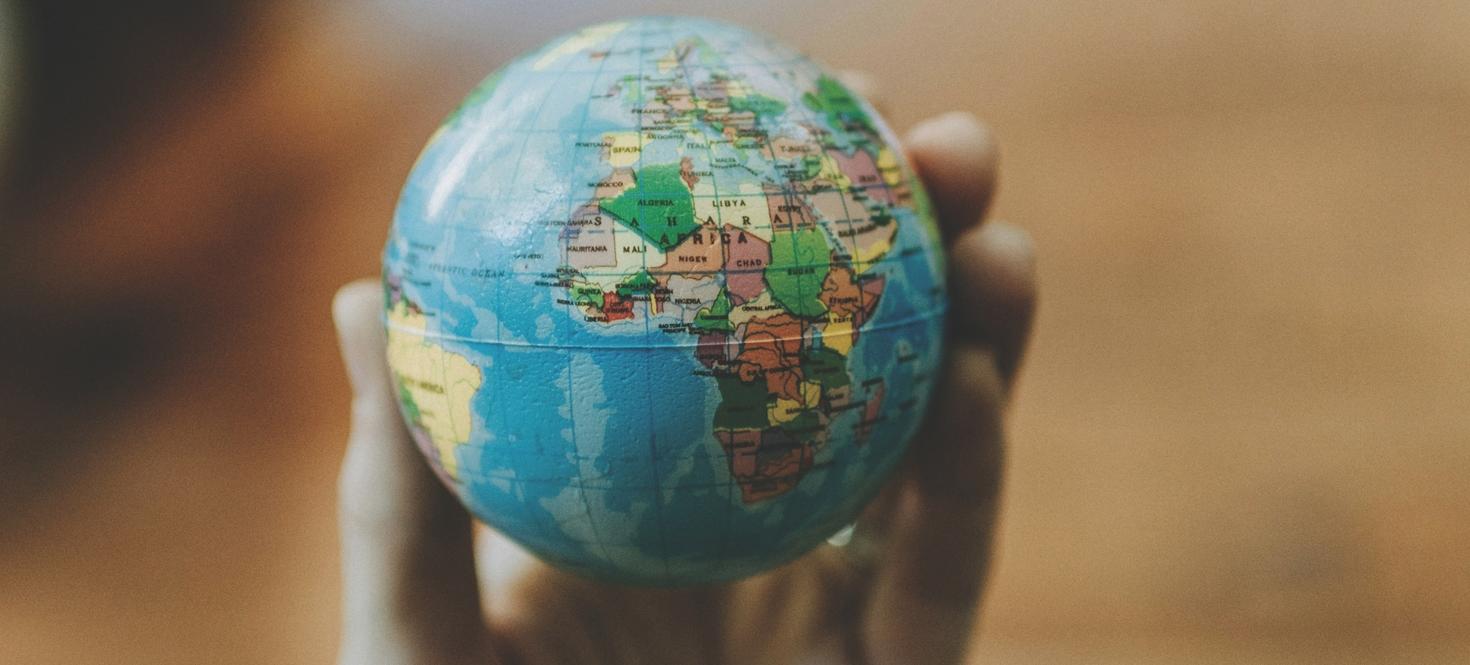 Petit globe terrestre avec vue sur l'Afrique, l'Europe et la pointe du Brésil, tenu dans la main d'une personne.