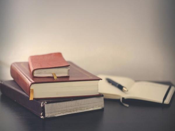 Trois livres empilés et un stylo posé sur un cahier ouvert.