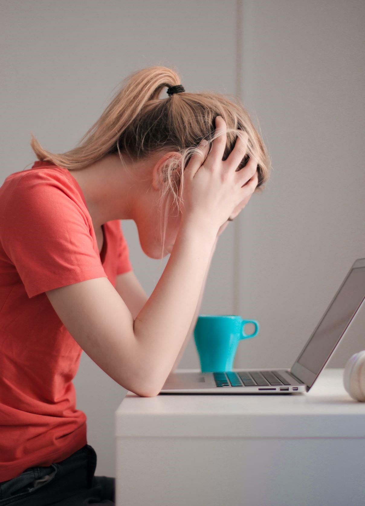 Une femme se tient la tête en regardant un écran d'ordinateur