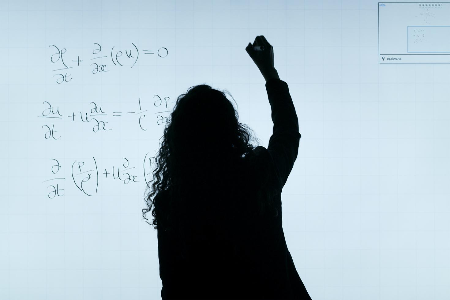 Un professeur est vu de dos alors qu'il écrit au tableau