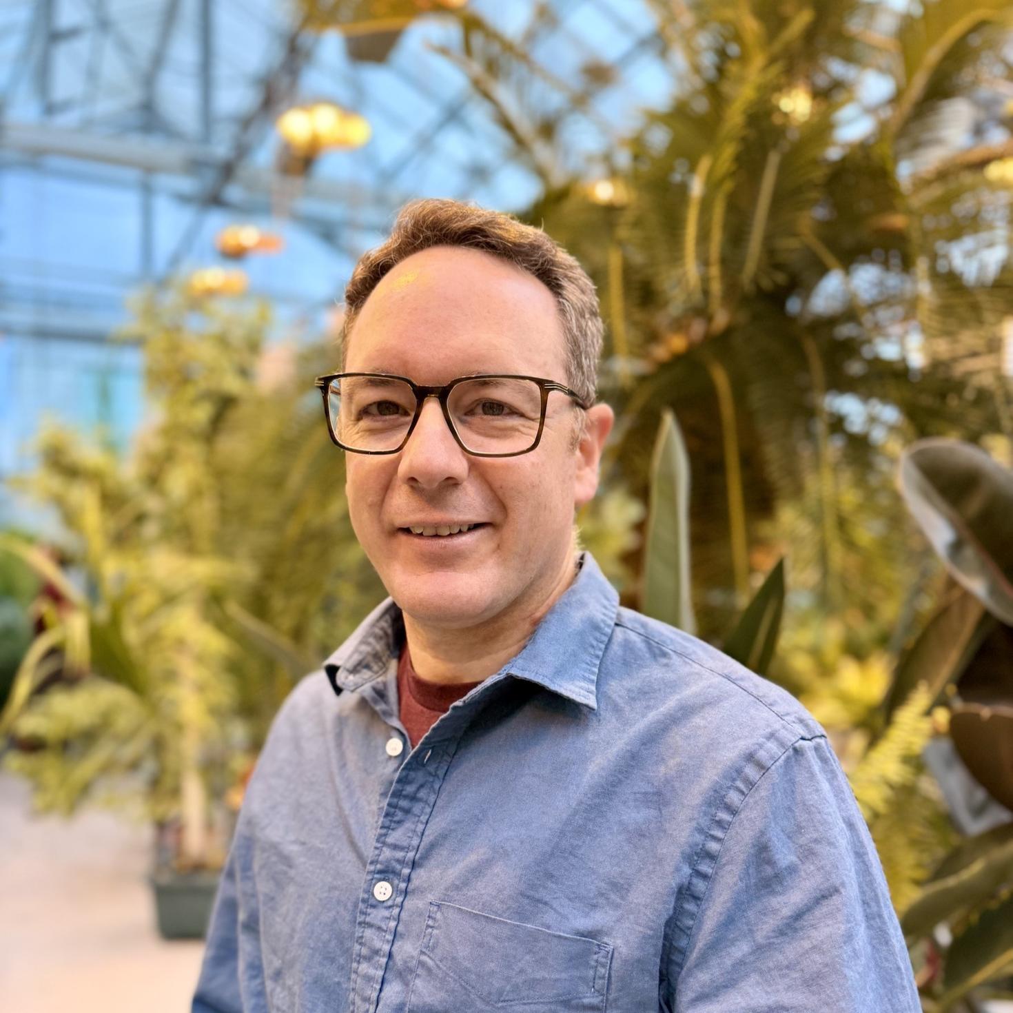 Marc Phillion posant devant des plantes dans la serre. 