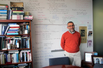 Professor standing in front of a white board next to a full bookshelf