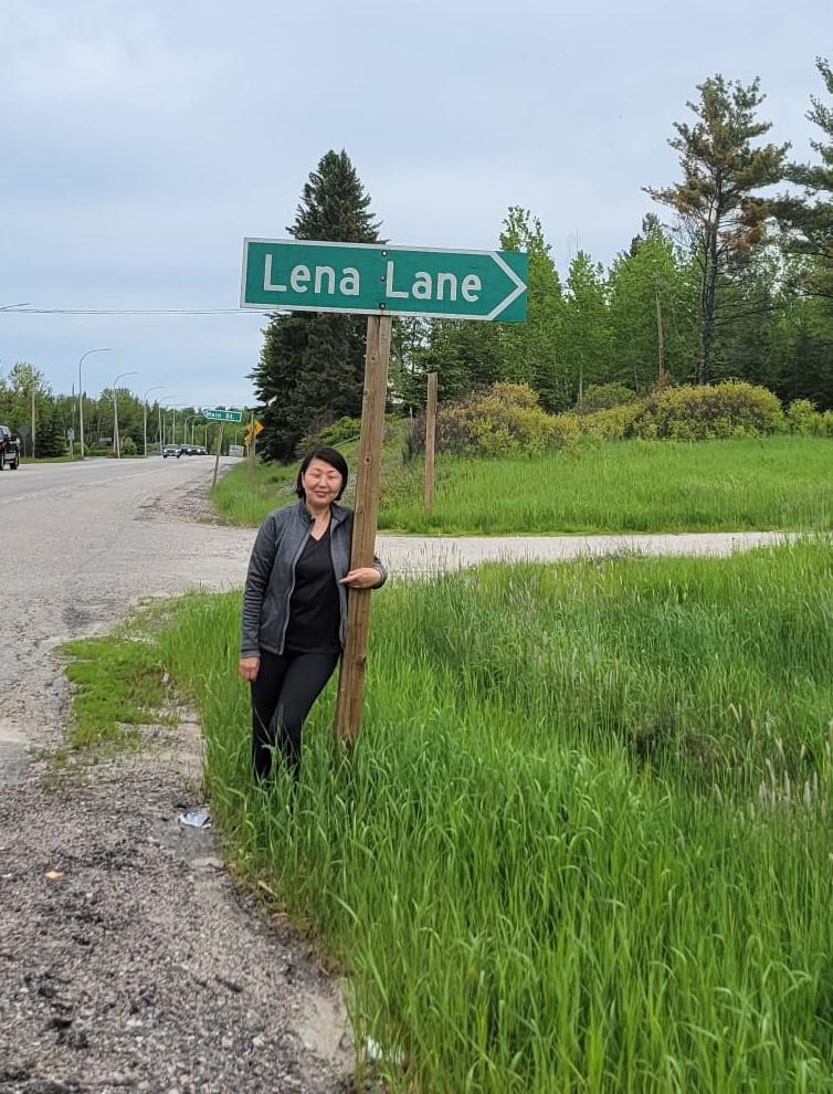 A woman named Lena stands underneath a road sign that says Lena Lane