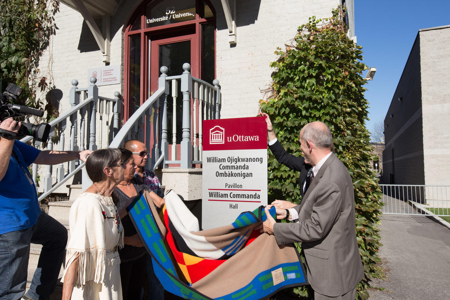 People removing a blanket covering a sign that says William Commanda Hall on it
