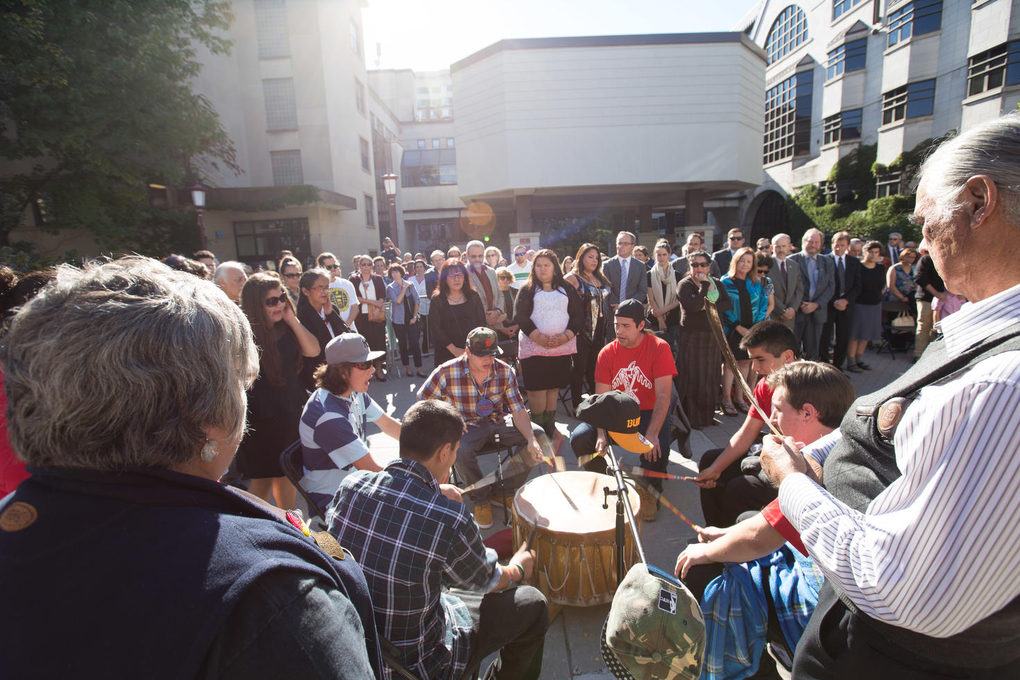 A group of Indigenous drummers surrounded by an onlooking crowd