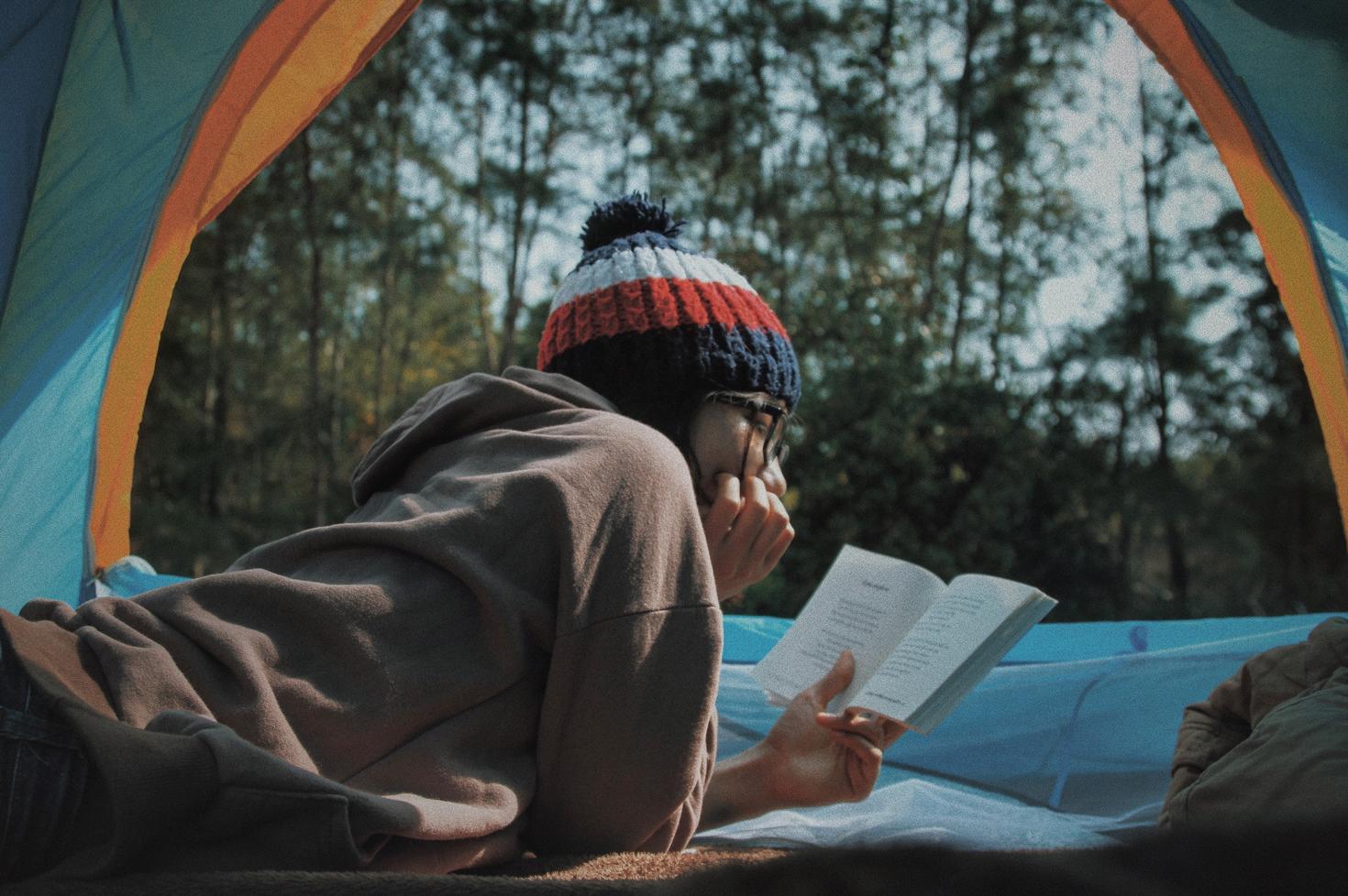 Girl reading a book in a tent in the forest