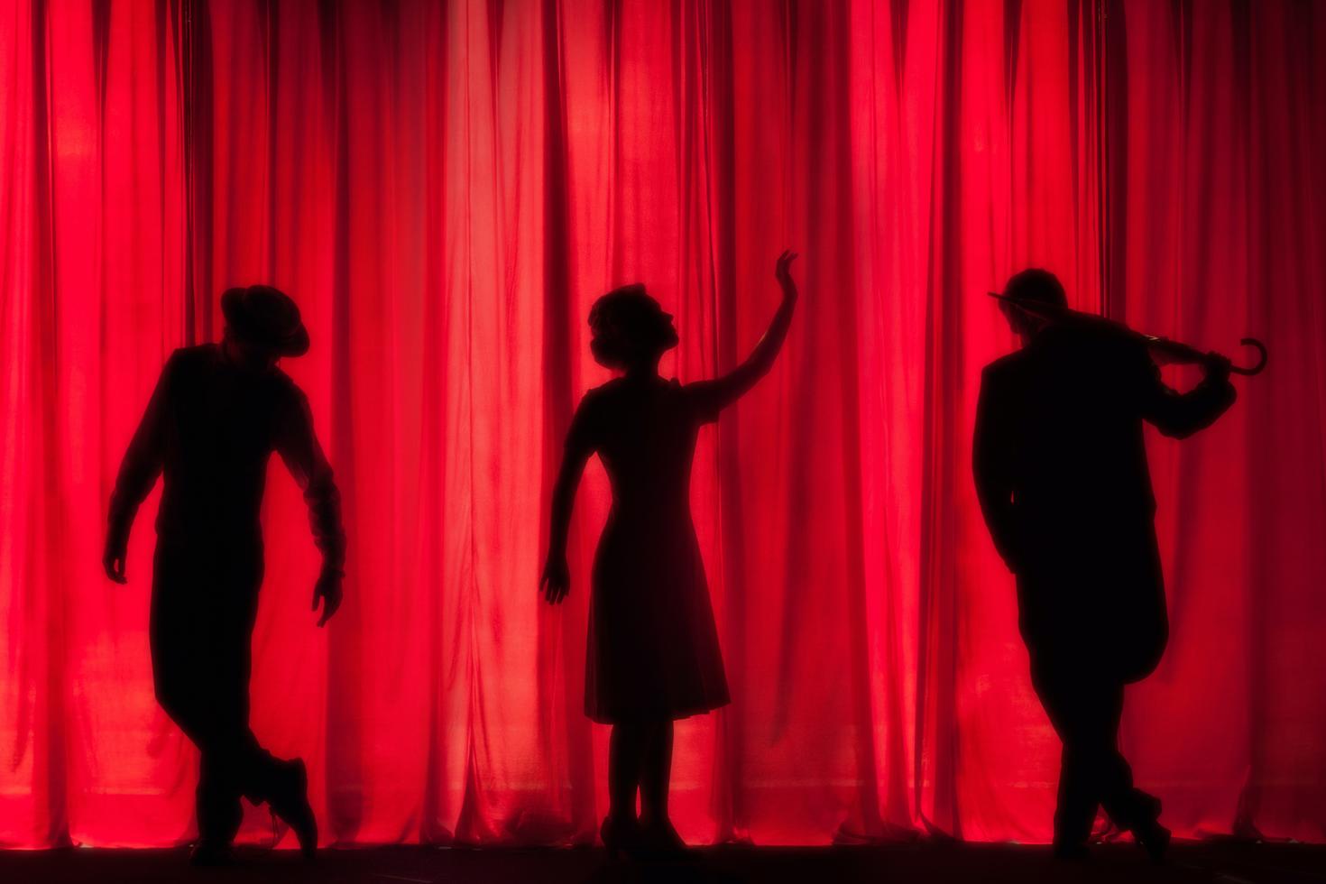 actors and actress on a theatre stage in front of a red curtain