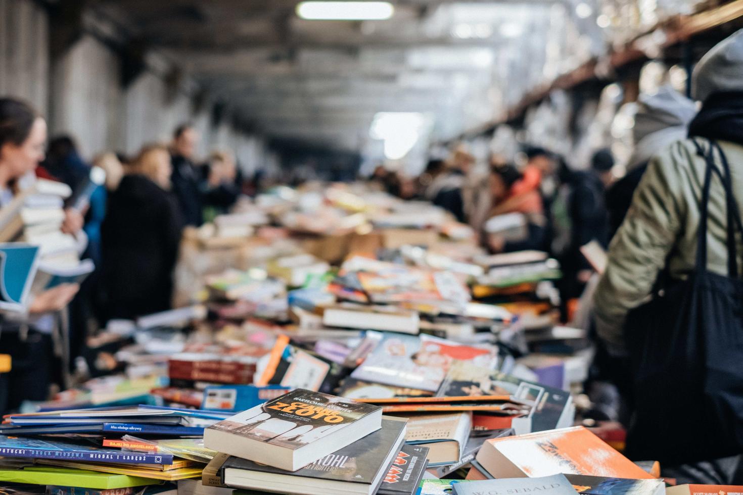 Tables full of unorganized books, with people lining the tables looking at the books