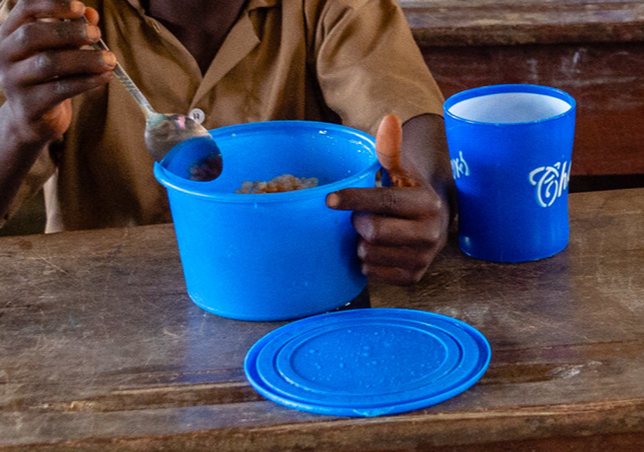 Phhoto of person's hands holding a meal in a blue container along with a cup