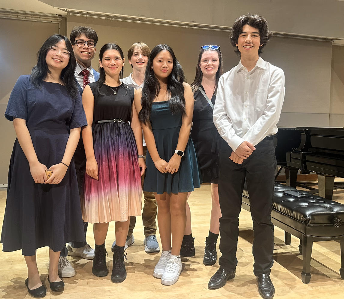 group of smiling piano students close to piano