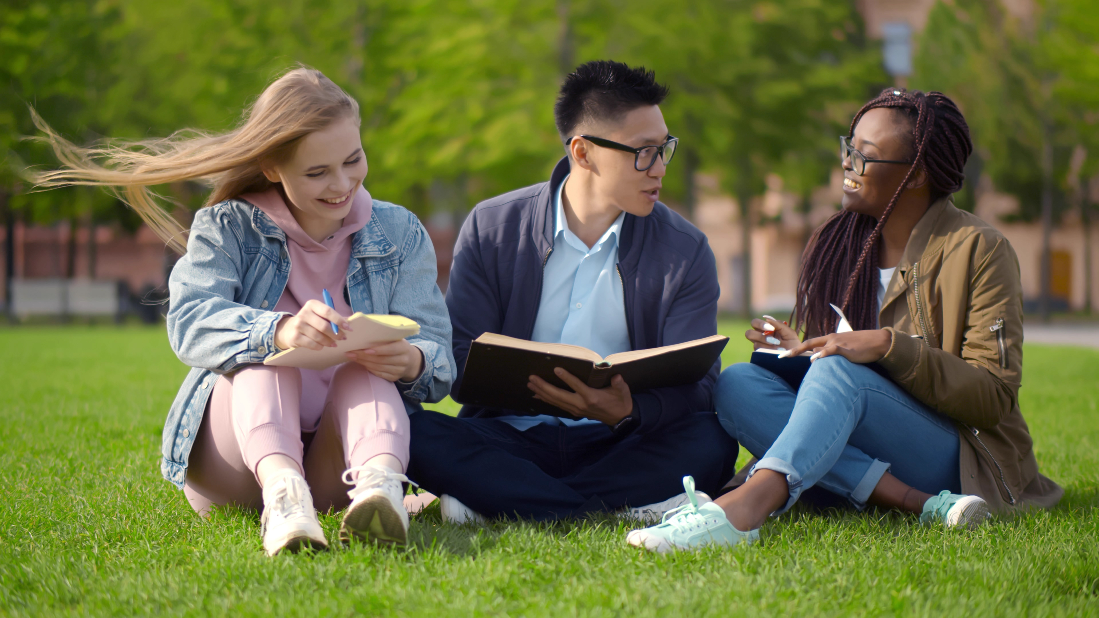 3 students sitting on the grass outside