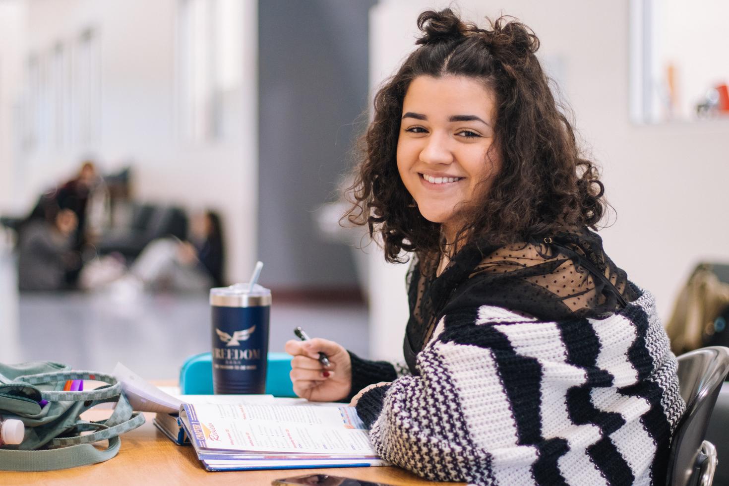 student looking at the camera and smiling while she is studying