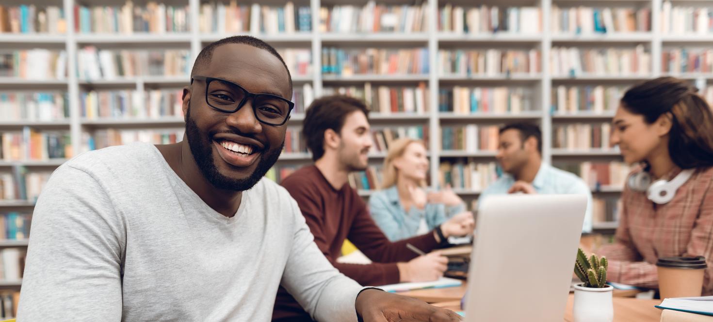 Person smiling, sitting in library with laptop