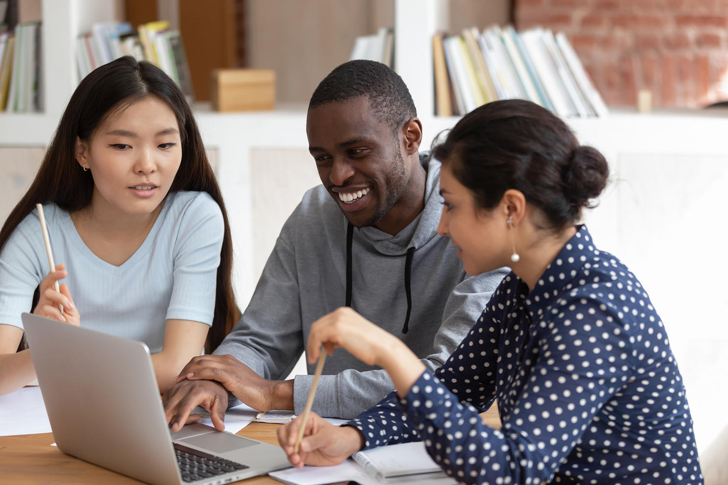 Three students sitting around a laptop, smiling.